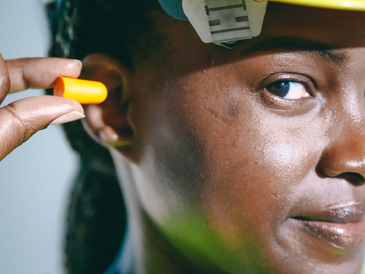 A close-up image of a woman inserting an earplug, wearing safety gear.